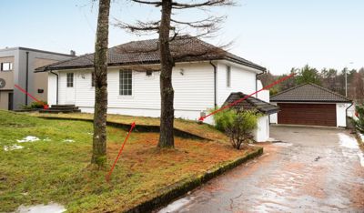 Fotografi av en hvit villa med garasje, sett fra siden. Bildet viser fasaden, taket, trær og omgivelser.