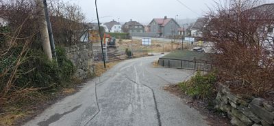 Fotografi av en vei som fører opp til et byggfelt med en grønt dekket container og en gulelastbil i bakgrunnen.