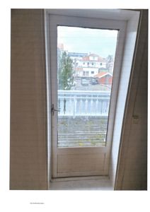 Fotografi av en hvit dør med glasspanel som leder ut til en balkong. I bakgrunnen ser man nabolaget med andre hus.