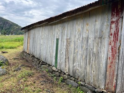 Fotografi av en lang, gammel bygning med trevegger og steinfundament, sett fra siden.