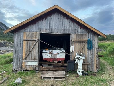 Fotografi av en gammel, trebygget båthol med en båt inni, sett fra front.
