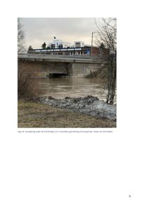 Fotografi av en vannføring under en bro (RV170) med en bygning i bakgrunnen.