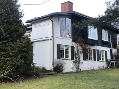 Fotografi av en toetasjes bolig med hvit og svart fasade, sett fra bakkenivå.