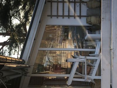 Fotografi av en bygning med store glassflater, hvite trekonstruksjoner og utemøbler.