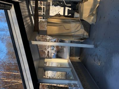 Fotografi av en utvendig del av en bygning, sannsynligvis en veranda eller en tilbygget del av huset, med snø på bakken.