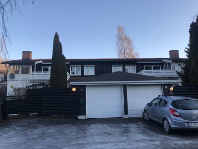 Fotografi av en rekkehusbebyggelse med garasje og bil foran.