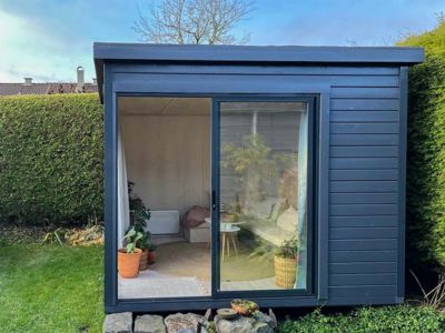 Fotografi av en ferdigbygd, mørk hytte eller uthus i en hage.