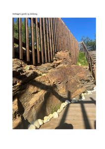 Fotografi av en utvendig detalj i en byggesak, spesifikt et gjerde og en skråning med stein og trapper.