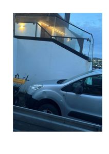 Fotografi av en moderne bygning med glassrailing, en hvit vegg og en bil parkert foran.