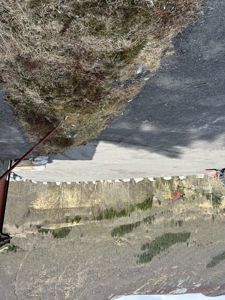 Fotografi av en byggeplass eller tomte med asfaltert overflate, en del av en bygning til høyre, og et fjellandskap i bakgrunnen.