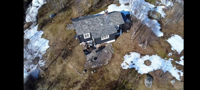 Luftfoto av en hytte på en fjellside med snøflekker.