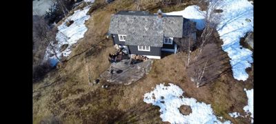Fotografi av en hytte sett fra luften (dronebilde). Bildet viser bygningen, omgivelsene med snø og terreng.
