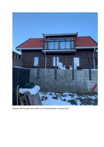 Fotografi av en ferdig eller nesten ferdig bygning sett fra siden, med en terrasse og en garasje.