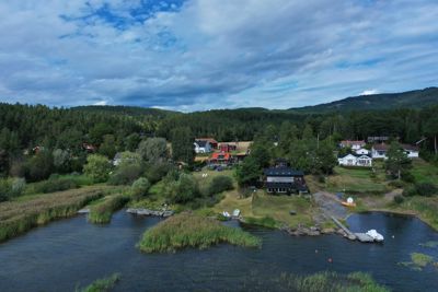 Fotografi av et boligområde ved vannet med flere hus, brygger og natur.