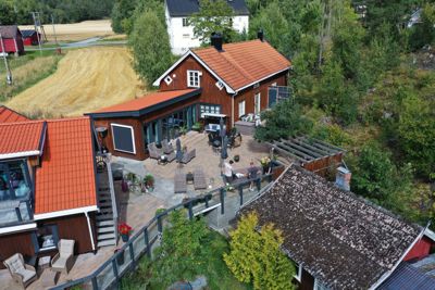 Fotografi av en eksisterende bygning med utvidelse, sett fra en høyde. Bildet viser fasade, tak, terrasse og omgivelser.