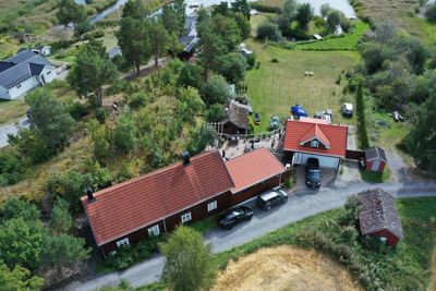 Luftfoto av en eiendom med flere bygninger, bilplassering og omgivelser.