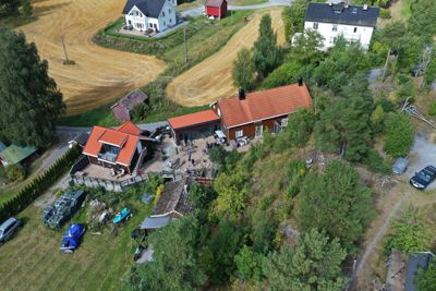 Luftfoto av en eiendom med flere bygninger, omgitt av skog og dyrket mark.