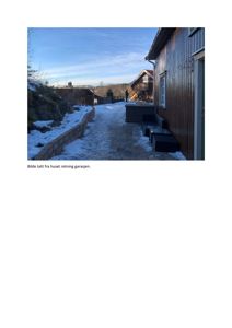 Fotografi av en uteplass med snø, en betongmur, en terrasse og en bygning i bakgrunnen.