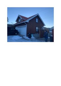 Fotografi av en ferdig eller nesten ferdig bygning (hus) med garasjeport, sett fra siden. Bildet viser også personer og snø på bakken.