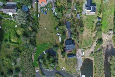 Luftfoto (dronebilde) av et boligområde med flere hus, hager, veier og vannløp.