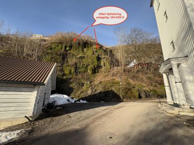 Fotografi av en bygning og en fjellside med en annotasjon om utført fjellsikring.