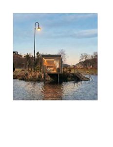 3D-visualisering av en liten hytte eller bryggehytte plassert på en holme i vannet, med lysende interiør og omgivende natur.