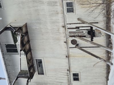 Fotografi av en hvit, tømmerbygd bygning sett fra siden (fasade). Bygningen har vinduer og et utvendig trappverk eller balkongkonstruksjon. Det er snø på bakken og takkantene.