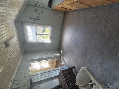 Fotografi av et gammelt, lite rom med flisete gulv, panelvegger og en liten vindu. Rommet ser ut til å være en del av en eldre bygning.