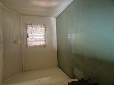 Fotografi av et tomt rom inne i en bygning, med hvite panelvegger, et vindu med gardin og en grønn farget vegg.