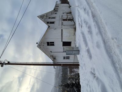 Fotografi av en hvit, toetasje bygning sett fra siden, med snø på bakken og en elektrisk stolpe i forgrunnen.