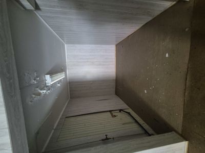 Fotografi av en inngangsgang eller trapp opp til etasjen, med synlig gulvkonstruksjon og vegger under ombygging.