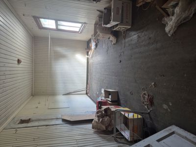 Fotografi av et innendørs rom, sannsynligvis en garasje eller lager, med hvite panelvegger, mørk gulvflate og taklykt.