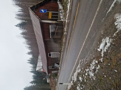 Fotografi av en rød, langbygget bygning (sannsynligvis en uthus eller garasje) sett fra siden langs en vei med snøflekker på bakken.