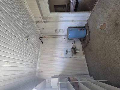 Fotografi av en innvendig hjørne i et bygg, som viser hvite panelvegger, gulv, en blå varmtvannsbereder og en vask.