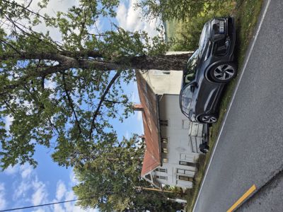 Fotografi av en hvit bygning med rustfarget tak sett fra en vei, med en bil parkert foran.