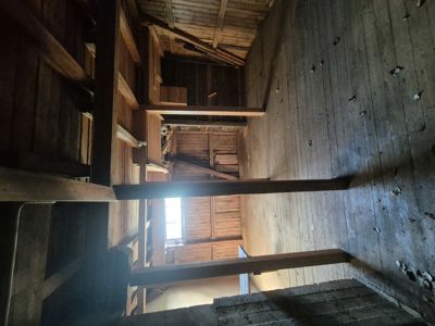 Fotografi av et gammelt trehus med synlig konstruksjon, gulv og takbjelker.