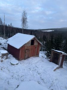 Fotografi av en rød skur og en mindre uthus i snø, med skog og fjell i bakgrunnen.