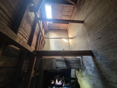 Fotografi av et gammelt, trolig ubebodd eller under restaurering, trehusinteriør sett fra et lavt perspektiv mot taket.