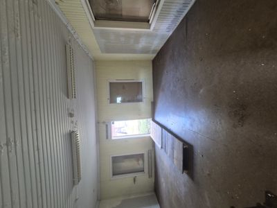 Fotografi av en tom, lang og smal romstruktur, sannsynligvis en korridor eller etasje i en bygning under ombygging eller renovering. Bildet viser gulv, vegger, tak og vinduer.