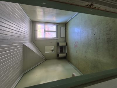 Fotografi av en liten, tom rom eller nisje med hvite panelvegger, et vindu og en liten hyllene.