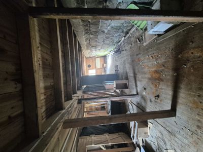 Fotografi av et gammelt, rustikt interiør, sannsynligvis et loft eller etasjeflokk i en bygning under restaurering eller ombygging. Bildet viser eksisterende trekonstruksjoner, gulv og vegger.
