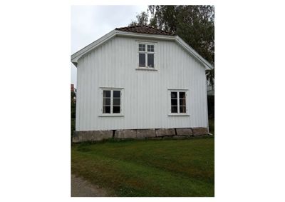 Fotografi av en hvit, trepanelert bygning med steinfundament og tre vinduer.