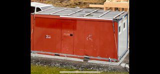 Fotografi av en ferdigstilt eller delvis ferdigstilt container eller modulær bygning med rød fasade og hvite detaljer.