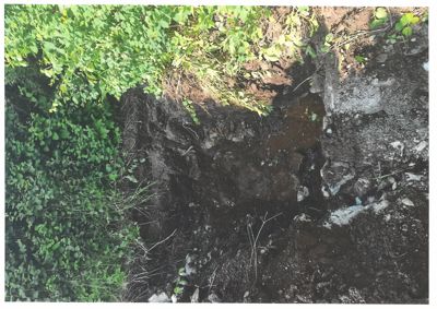 Fotografi av en grøft eller utgravet område med jord, steiner og vegetasjon.