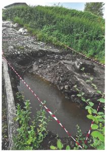 Fotografi av en utgravd grøft eller kanal med vann, omgitt av vegetasjon og en betongkant.