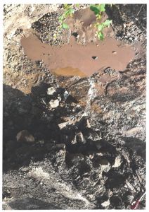 Fotografi av en grøft eller utgravet område med mudder, steiner og en liten vannlomme.