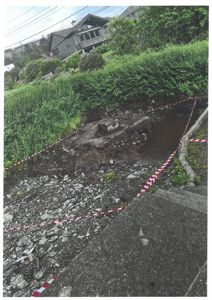 Fotografi av en utgravet eller forurenset grøft på en tomt, med advarselstape og nabohus i bakgrunnen.