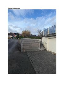 Fotografi av en ferdig bygd støttemur i grå steinblokker, med tilhørende trapp og garasjeport.