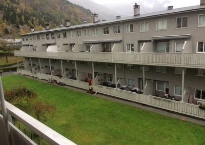 Fotografi av en fleretasjes bebyggelse sett fra et høyere nivå, med grønt område og bakke i forgrunnen.