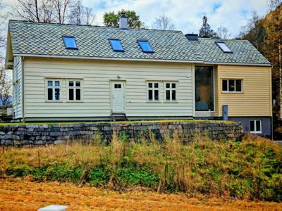 Fotografi av en eksisterende eller ferdigstilt enebolig sett fra siden, med omgivende natur og terreng.